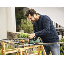 Man schuurt metalen rooster met een excentrische schuurmachine buitenshuis
