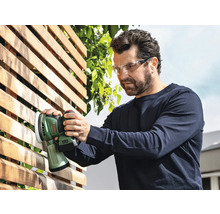Man schuurt een houten schutting met een Bosch accu-excentrische schuurmachine en draagt een veiligheidsbril.