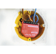 Gedetailleerde opname van een Shelly Gen3 relais in een gele inbouwdoos met elektrische leidingen.