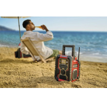 Een Einhell bouwradio op het strand met een persoon op de achtergrond die van een drankje geniet.