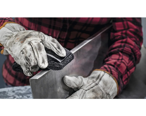 Iemand maakt een stuk metaal schoon met een borstel.