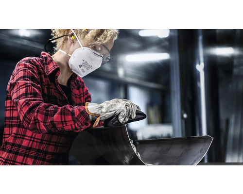 Een persoon met een beschermend masker, veiligheidsbril en handschoenen bewerkt een werkstuk.