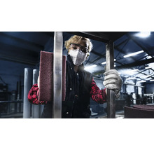 Een persoon met een veiligheidsbril en een ademhalingsmasker houdt een schuurvlies vast in een werkplaats.