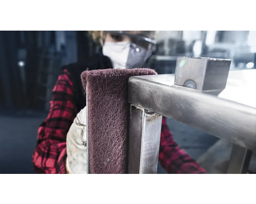 Een persoon polijst een metalen constructie met een schuurvlies.