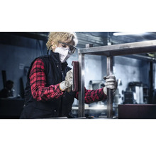 Vrouw schuurt metalen frame met schuurvlies, draagt beschermende kleding