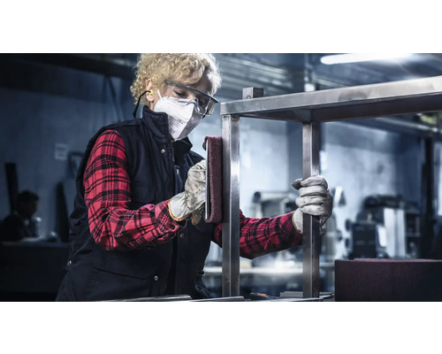 Vrouw schuurt metalen frame met schuurvlies, draagt beschermende kleding