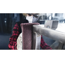 Een persoon reinigt een metalen constructie met een schuurvlies.