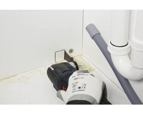 Een persoon gebruikt een multifunctioneel gereedschap om een kast te snijden in de buurt van een afvoer.