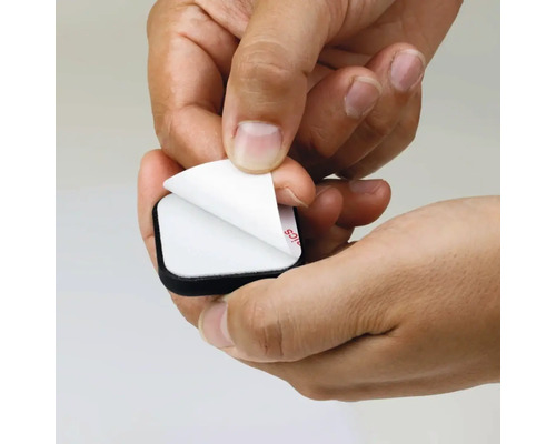 Een hand trekt de beschermfolie van een zelfklevende meubelglijder af.