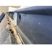 Detailopname van een dakgoot met bitumen afdichting en afvoerpijp