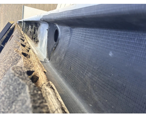 Detailopname van een dakgoot met bitumen afdichting en afvoerpijp