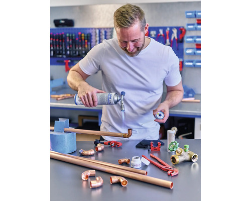 Man soldeert koperen buizen met een gasbrander en gereedschap op een tafel.
