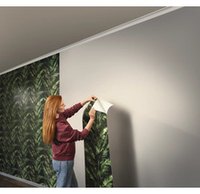 Vrouw brengt een behang met plantenpatroon op een muur aan.
