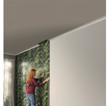 Vrouw brengt een groen bladerbehang aan in een kamer.
