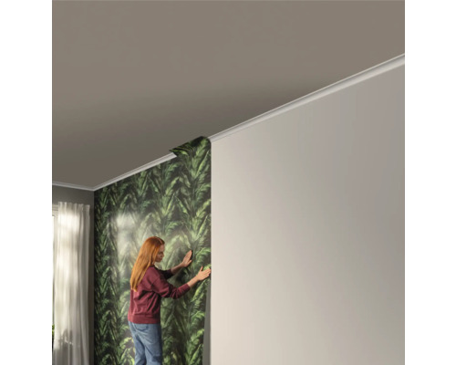 Een vrouw behangt een muur met groen bladerbehang in een heldere kamer.