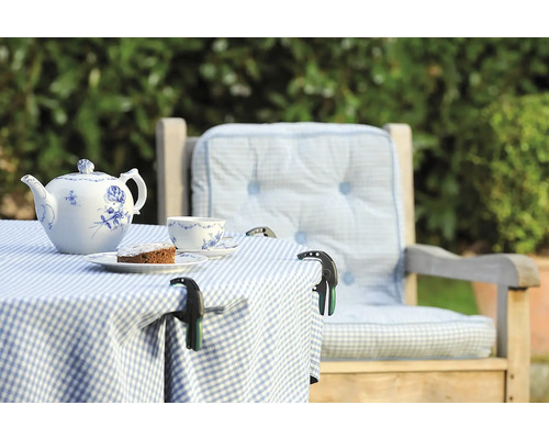 Gedekte tuintafel met theepot, kopje, taart en tafelkleedklemmen op een geruite tafelkleed naast een stoel met kussens