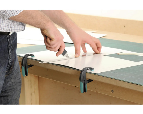 Het snijden van een plastic plaat met een stanleymes en een liniaal, vastgezet met een klem.