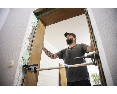 Vakman monteert een houten deurkozijn met een richtlat