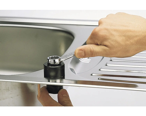 Een hand monteert met een moersleutel een spoelbakbevestigingsblok aan een spoelbak.