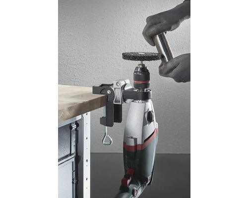 Een boormachine met een slijpopzetstuk, bevestigd aan een werkbank, wordt gebruikt om een stuk metaal te bewerken.