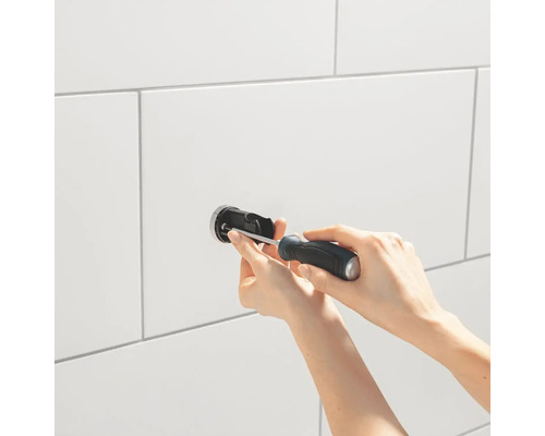 Installatie van een kraan in de badkamer met een schroevendraaier op witte tegels.