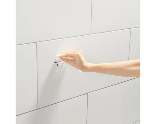 Een hand veegt een Grohe bedieningspaneel af op een betegelde muur.