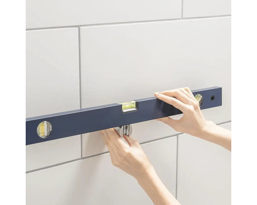 Een waterpas wordt aan een betegelde muur bevestigd.