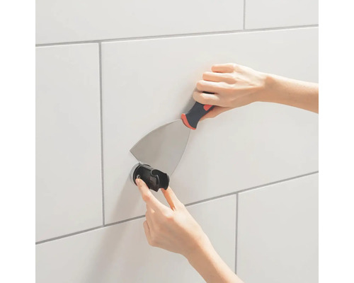 Montage van een douchekophouder met een plamuurmes op een betegelde muur