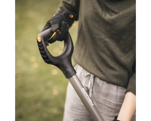 Gedetailleerde opname van een Fiskars-spadehandvat, vastgehouden door iemand met werkhandschoenen.