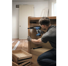 Een persoon monteert met een accuschroevendraaier een ladegeleider aan een houten kast.