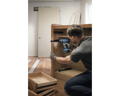 Een persoon monteert met een accuschroevendraaier een ladegeleider aan een houten kast.