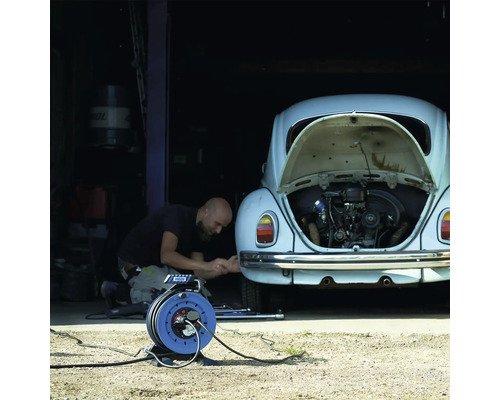 Een persoon repareert een auto in een garage met een haspel.