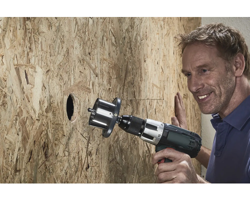 Een man boort een gat in een houten plaat met een gatzagen.