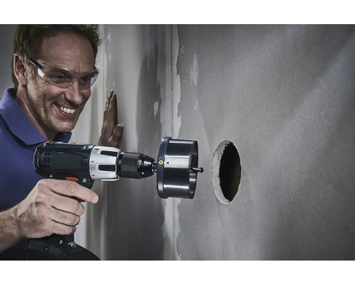 Man boort met een gatenzaag een gat in een muur