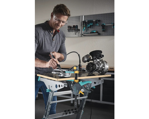 Man met veiligheidsbril bewerkt metalen onderdeel op een Wolfcraft werkbank met een multifunctioneel gereedschap.