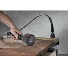 Persoon gebruikt een lamellenborstel op een houten plank, aangedreven door een boormachine.
