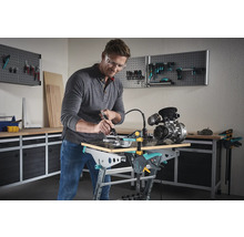 Man werkt met een multifunctioneel gereedschap aan een werkstuk op een Wolfcraft werkbank in een werkplaats.