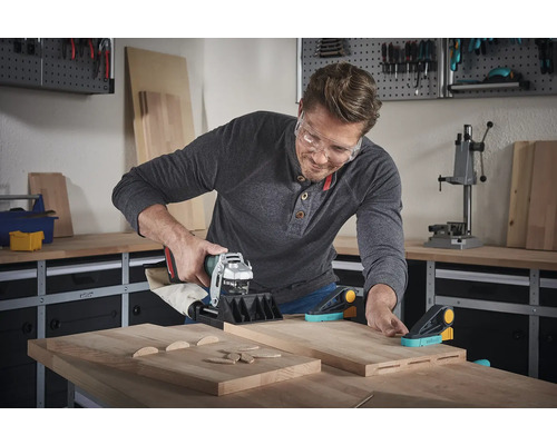 Een man gebruikt een lamellenfrees op houten planken in een werkplaats.