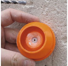 Close-up van een persoon die werkt met een boor en een oranje stofkap