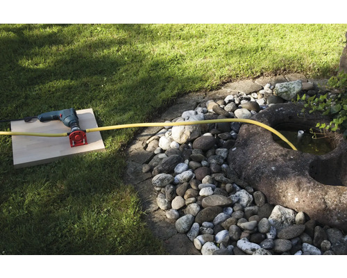 Een boormachine met wateraansluiting en slang in de tuin.