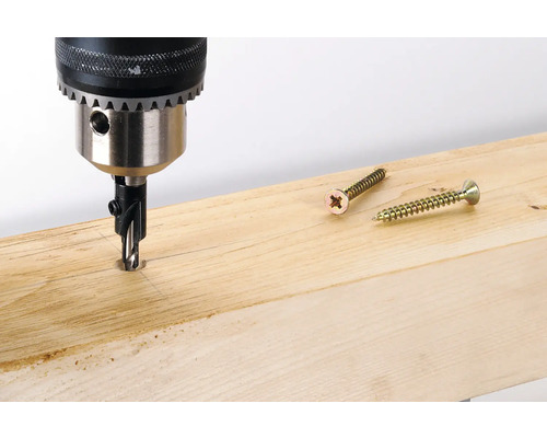 Boormachine boort gat in een houten plank, schroeven liggen klaar