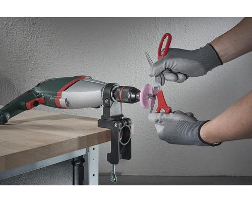 Een boormachine met een gemonteerd slijphulpstuk wordt gebruikt om een schaar te slijpen.