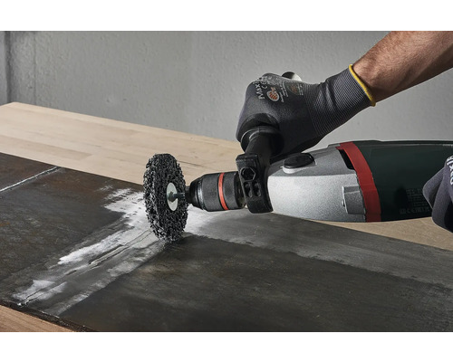 Een staalborstel wordt met een boormachine op een houten plank gebruikt.