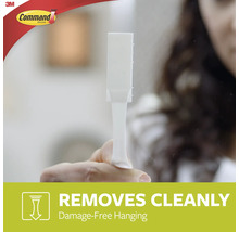 Een persoon houdt een witte Command kleefstrip in de hand, die schoon verwijderbaar is.