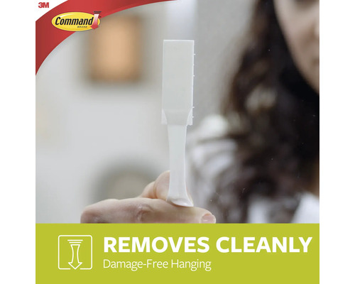 Een persoon houdt een witte Command kleefstrip in de hand, die schoon verwijderbaar is.