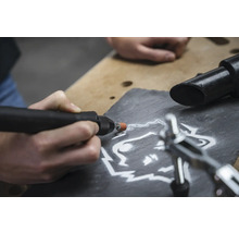 Close-up van een persoon die met een multifunctioneel gereedschap een wolfsmotief in een leisteen graveert.
