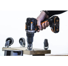 Een hand houdt een draadloze schroevendraaier van het merk Worx vast tijdens het bevestigen van een zwenkwiel aan een houten plank.