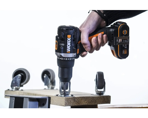 Een hand houdt een draadloze schroevendraaier van het merk Worx vast tijdens het bevestigen van een zwenkwiel aan een houten plank.