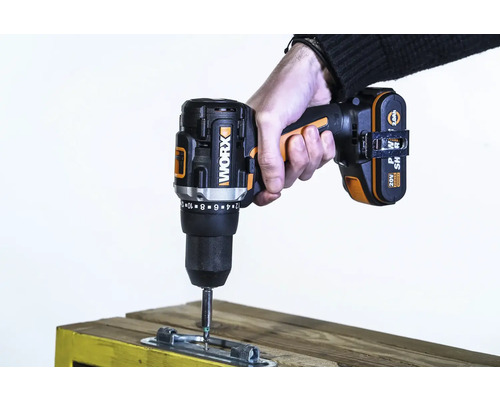 Een draadloze accuschroevendraaier van het merk Worx wordt gebruikt om een metalen plaat aan een stuk hout te bevestigen.