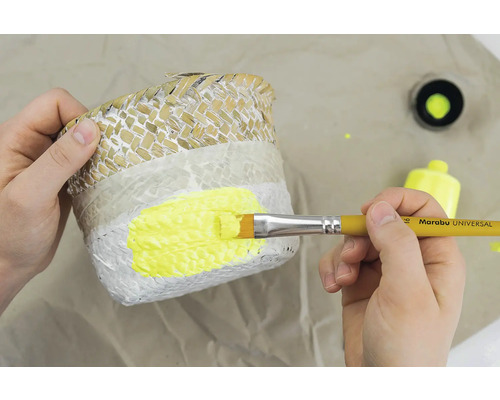 Een persoon schildert een plantenmand met een penseel en gele verf.